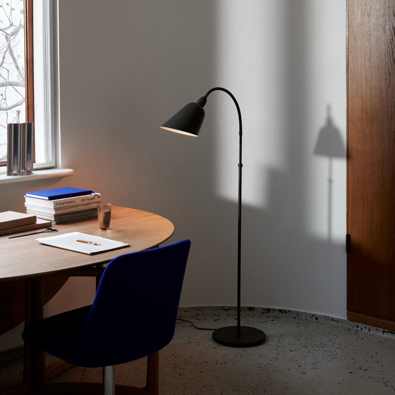 "Black floor lamp with a sleek curved design, casting a soft shadow on a light gray wall."