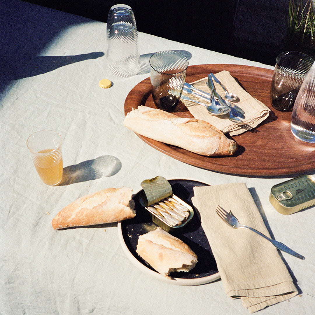Rustic wooden tray with beige tablecloth, black plate, green napkin, and clear glassware showcasing warm tones.