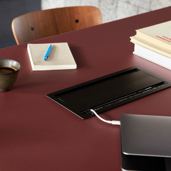 "Black charging pad on deep red table, with blue pen and beige notebook for stylish workspace contrast."
