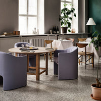 Modern dining room featuring light purple chairs, wooden table, and earthy green walls with subtle textures.