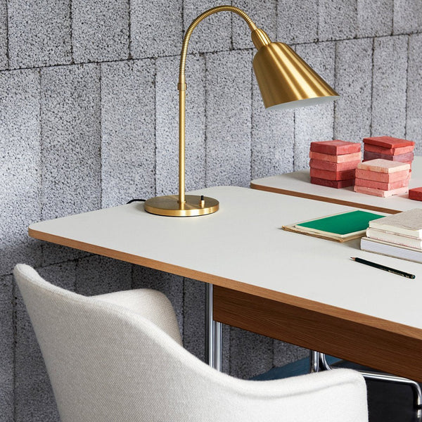 Gold desk lamp with a white and wood desk, featuring pink and green stationery against a textured gray wall.
