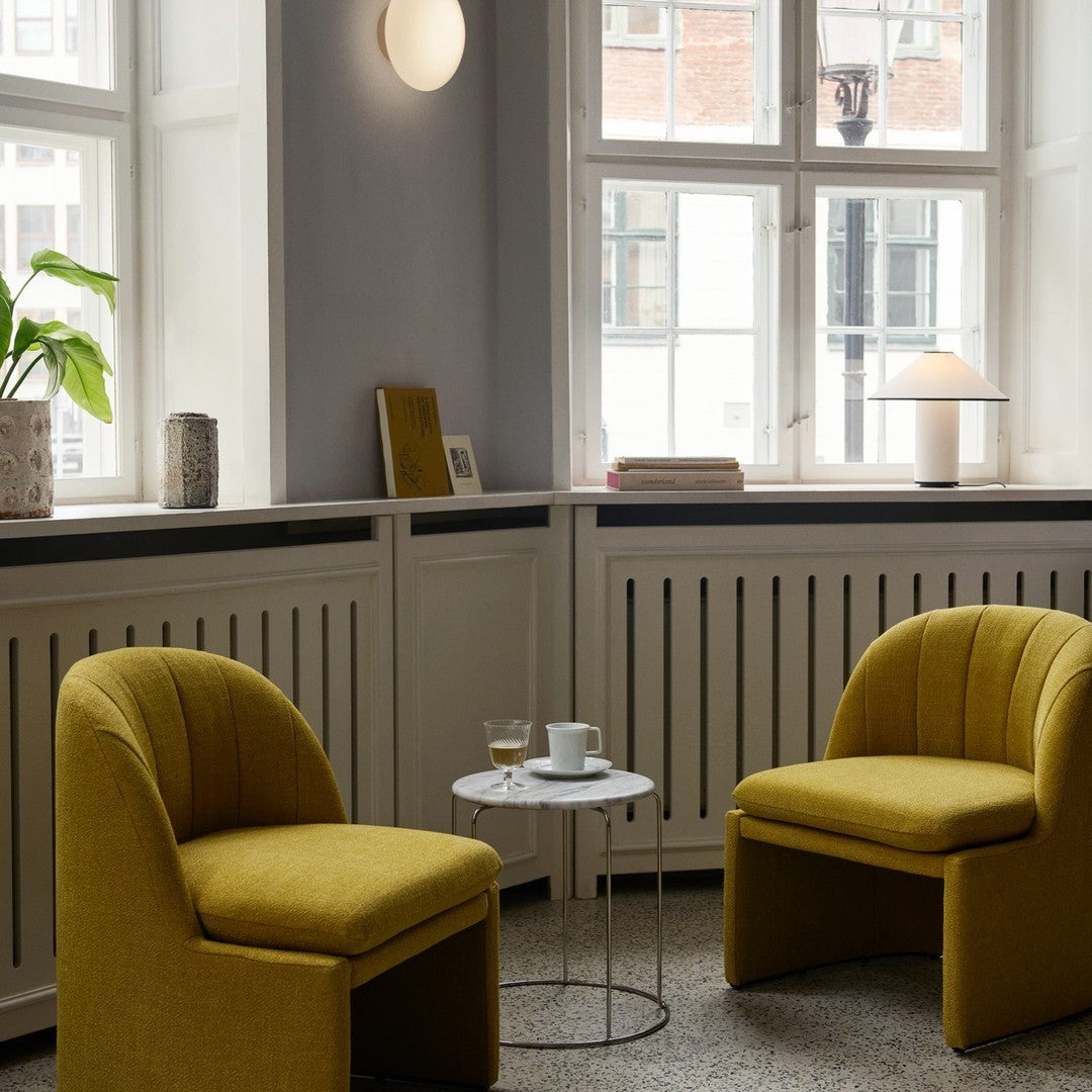 Two mustard yellow chairs with quilted patterns in a modern, minimalist interior space, featuring light gray walls.