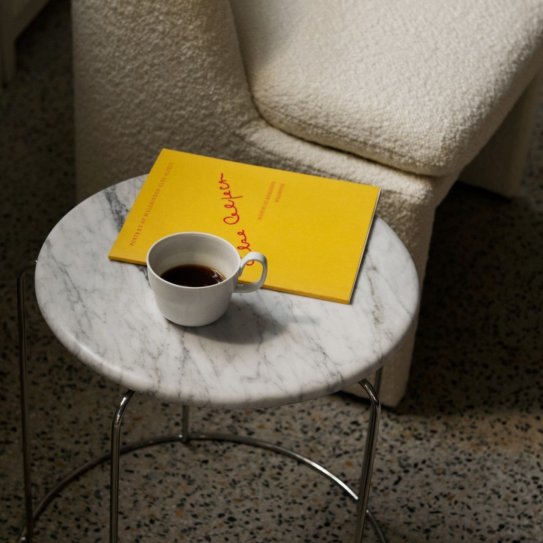 White marble coffee table with a yellow book and a white cup, showcasing a modern, minimalistic color palette.