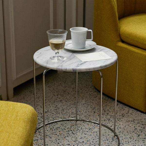 Marble top side table with gray veining, silver legs, and a vibrant yellow chair in the background.