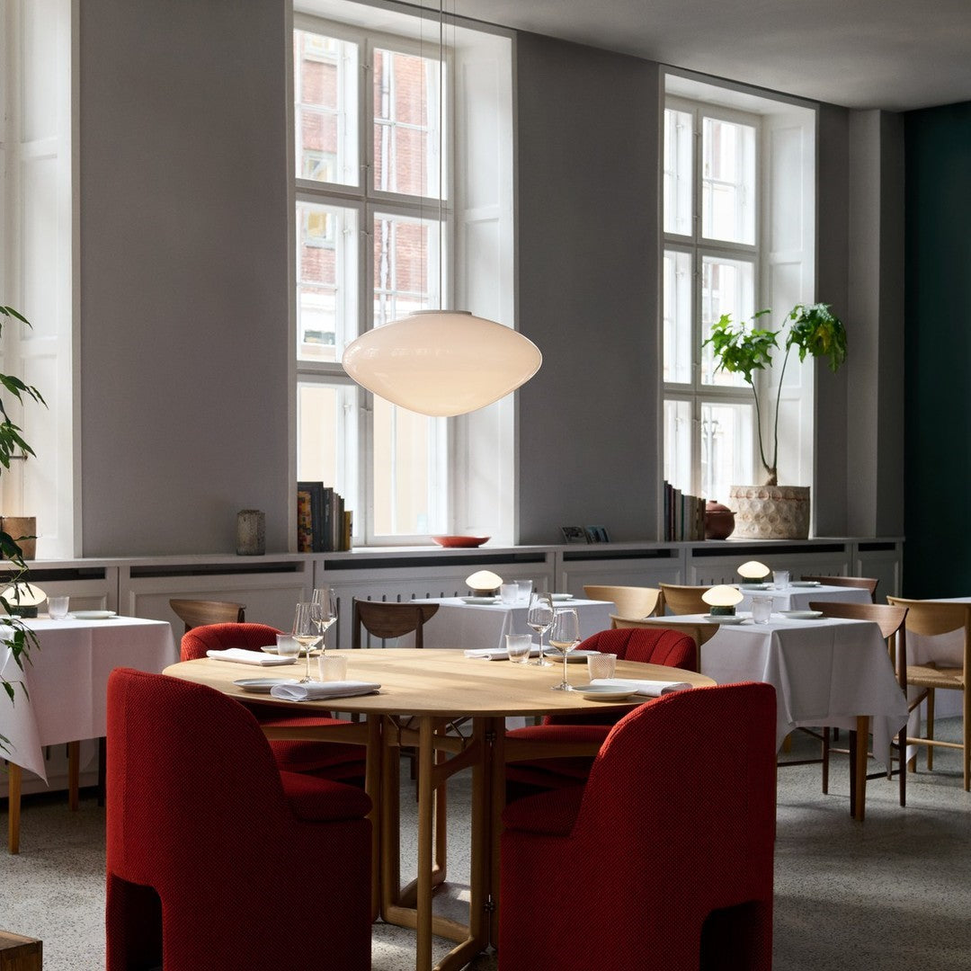 Modern dining room featuring deep red chairs, white table linens, and neutral gray walls with green accents.