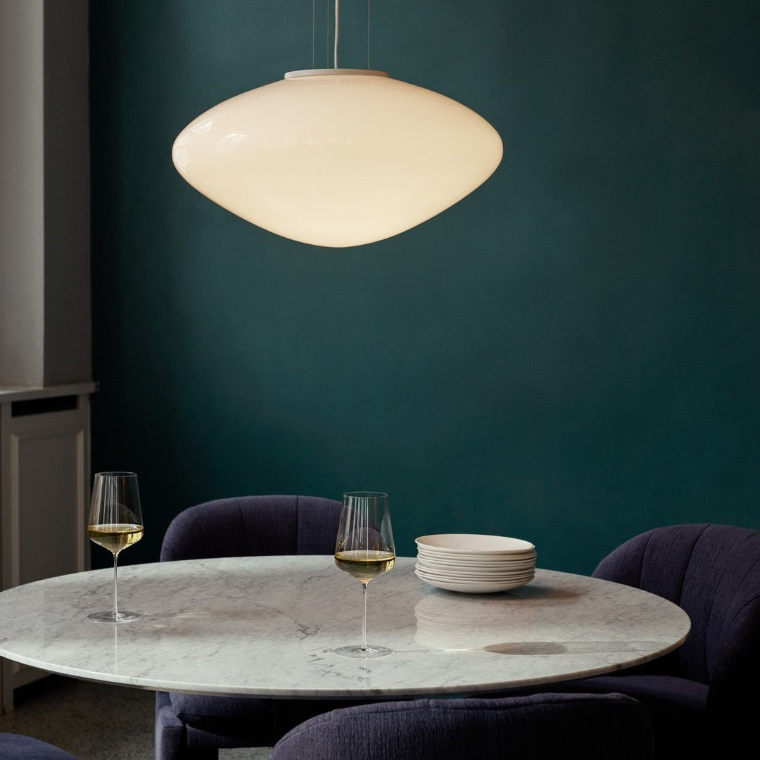 Modern white pendant light against a deep teal wall, with textured dark purple chairs and a marble table.