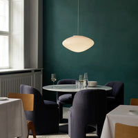 Soft white pendant light against a deep green wall, complemented by dark blue chairs and a marble table.