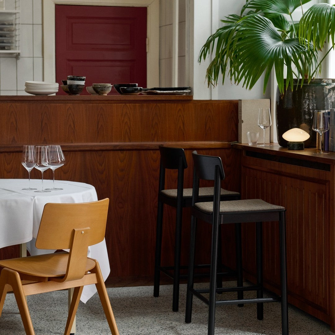 "Warm wood tones, crisp white tablecloth, and bold red door with green palm accents create a modern, inviting atmosphere."