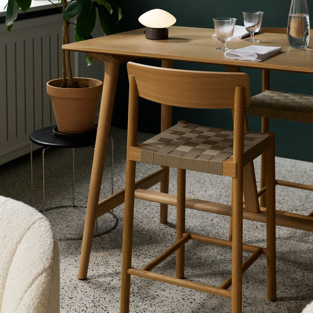 Wooden table with beige and brown patterned chair, green walls, and textured grey floor, accented by soft lighting.