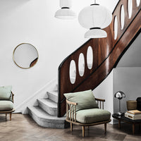 Modern staircase with wood accents, soft green armchairs, and neutral tones, complemented by round light fixtures.