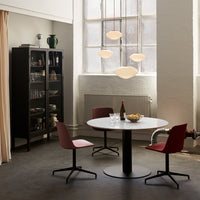 Modern dining setup featuring a white round table, burgundy chairs, and warm pendant lights against a neutral backdrop.
