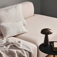 Light pink sofa with textured cushions, contrasting neutral throw blanket, and a sleek dark metal lamp on a round table.