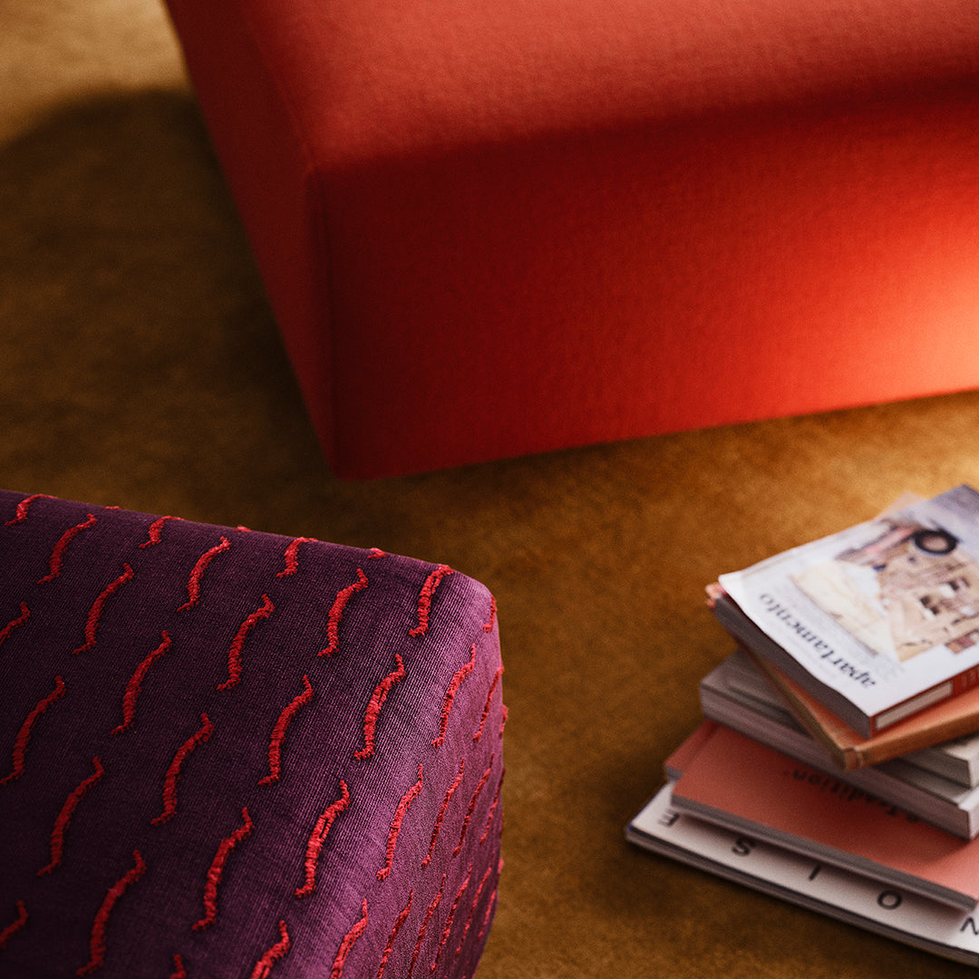 Red and purple textured ottomans against a warm gold backdrop, featuring wavy patterns and stacked magazines.