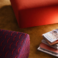 Red and purple textured ottomans against a warm gold backdrop, featuring wavy patterns and stacked magazines.