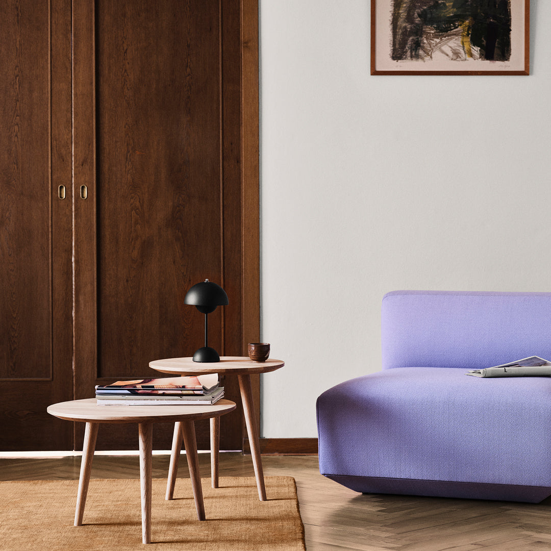 Lavender sofa with rounded edges, paired with light wood accent tables and a textured beige area rug.