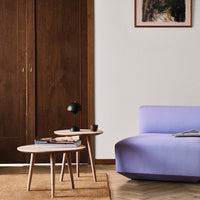 Lavender sofa with rounded edges, paired with light wood accent tables and a textured beige area rug.