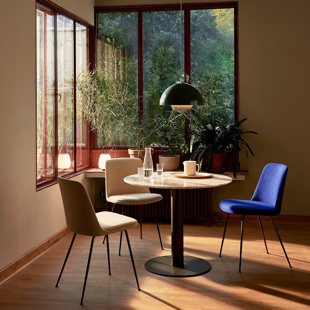 "Modern dining chairs in beige and blue, paired with a round white table under a green pendant lamp in a sunlit room."
