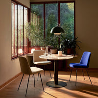 "Modern dining chairs in beige and blue, paired with a round white table under a green pendant lamp in a sunlit room."