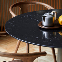 Black marble table with white veining, surrounded by wooden chairs, featuring a silver teapot and yellow lemon accents.