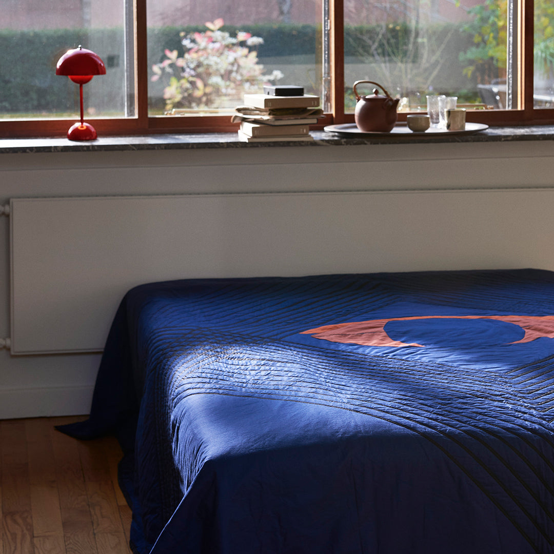 Navy quilt with circular orange pattern and textured lines, featured in a cozy indoor setting.