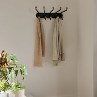 Black wall-mounted coat rack with natural wood knobs holding beige and light gray towels against a neutral wall.