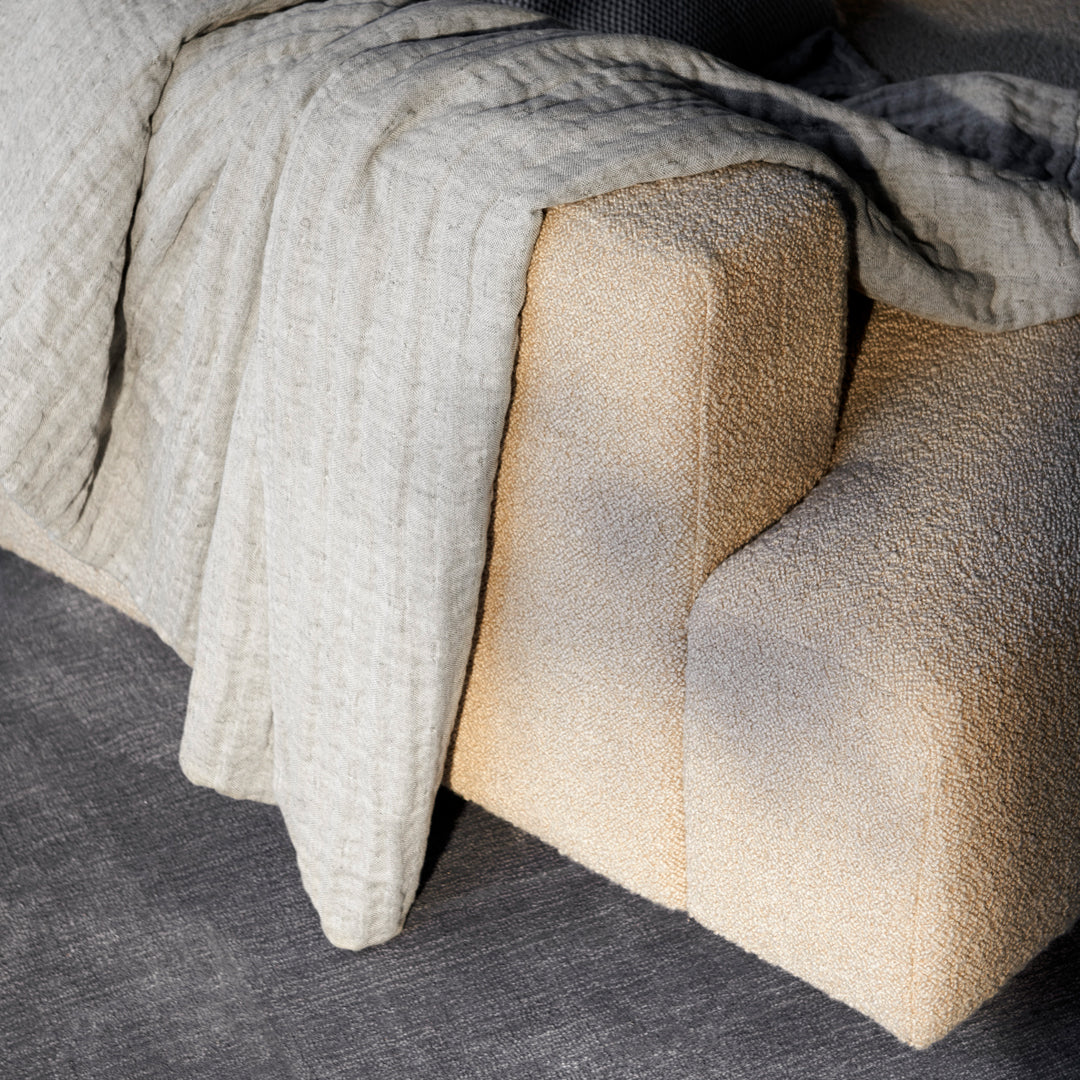 Textured beige fabric draped over a soft cream-colored couch, set against a dark gray background.