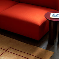 Vibrant red couch with a smooth texture, paired with a round dark wood table and a woven tan rug featuring red geometric lines.
