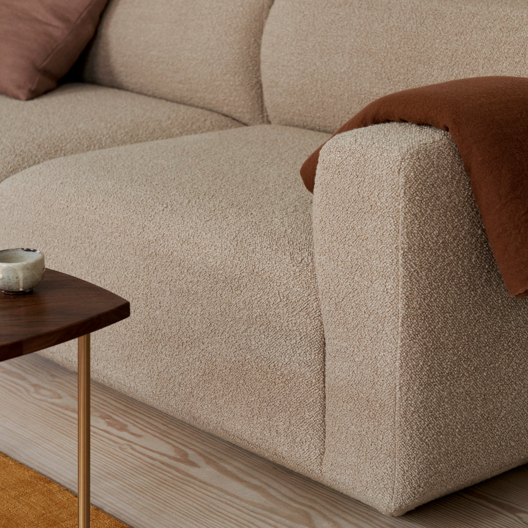 Beige textured sofa with rounded arms, complemented by a rust-colored throw blanket. Cozy and modern design.