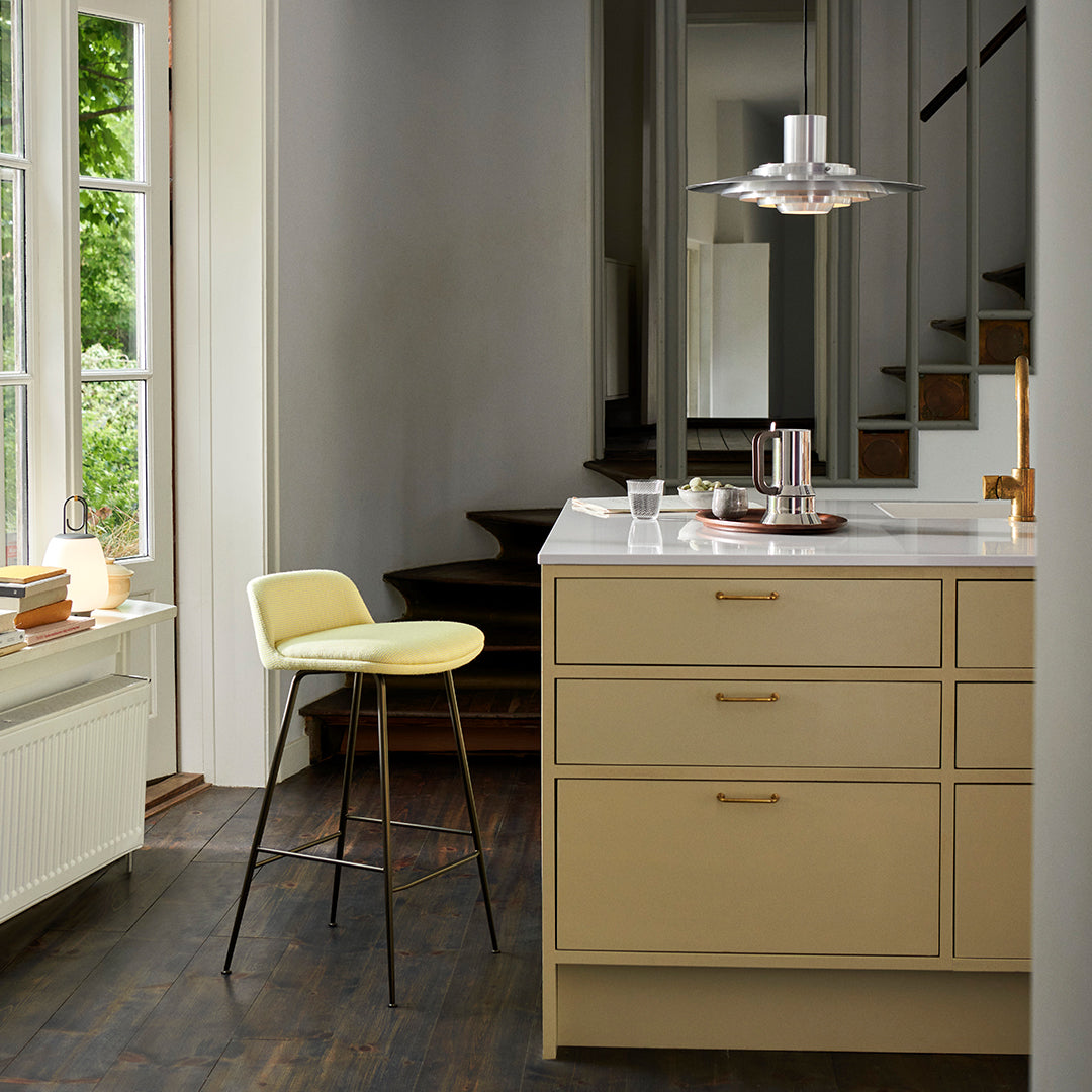 Light yellow stool against a warm beige kitchen island with a dark wooden floor, featuring a sleek silver pendant light.