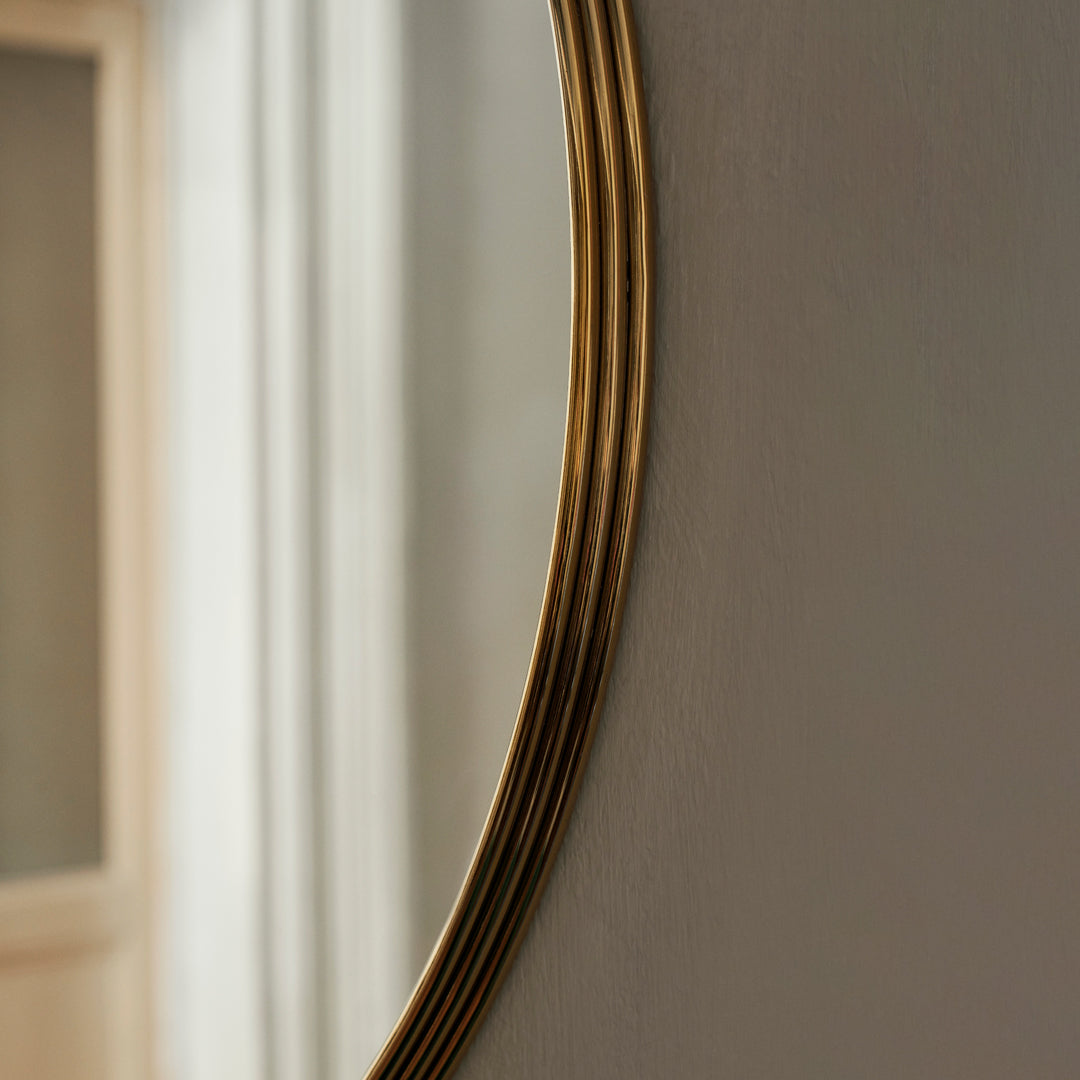 Gold-accented curved mirror with a sleek, minimalist design against a soft, neutral backdrop.