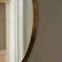 Gold-accented curved mirror with a sleek, minimalist design against a soft, neutral backdrop.