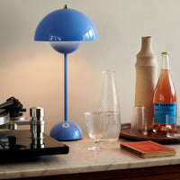 Blue lamp with a glossy finish beside clear glassware and earthy-toned decor, enhancing a stylish tabletop arrangement.