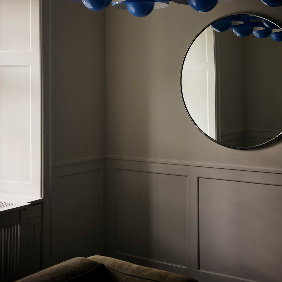 Round mirror reflecting light gray walls and dark furniture, accented by blue decorative elements above.