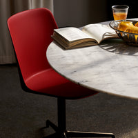 Red chair beside a round marble table with a casual book and a bowl of fruit, showcasing a sleek, modern design.