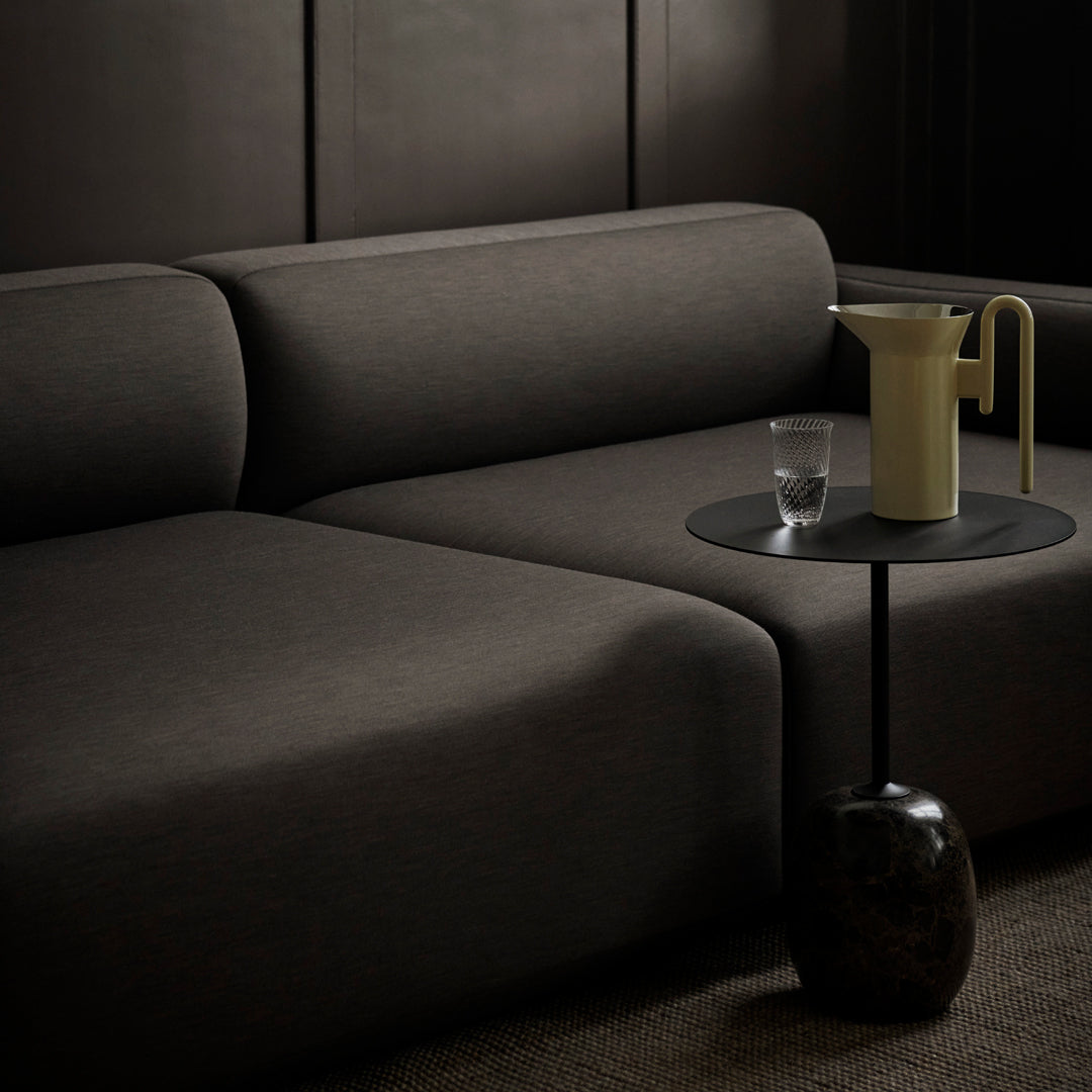 Modern black sofa with clean lines, paired with a minimalist yellow pitcher and glass on a dark, circular table.