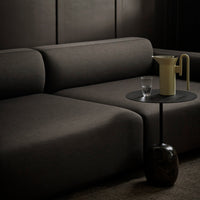 Modern black sofa with clean lines, paired with a minimalist yellow pitcher and glass on a dark, circular table.