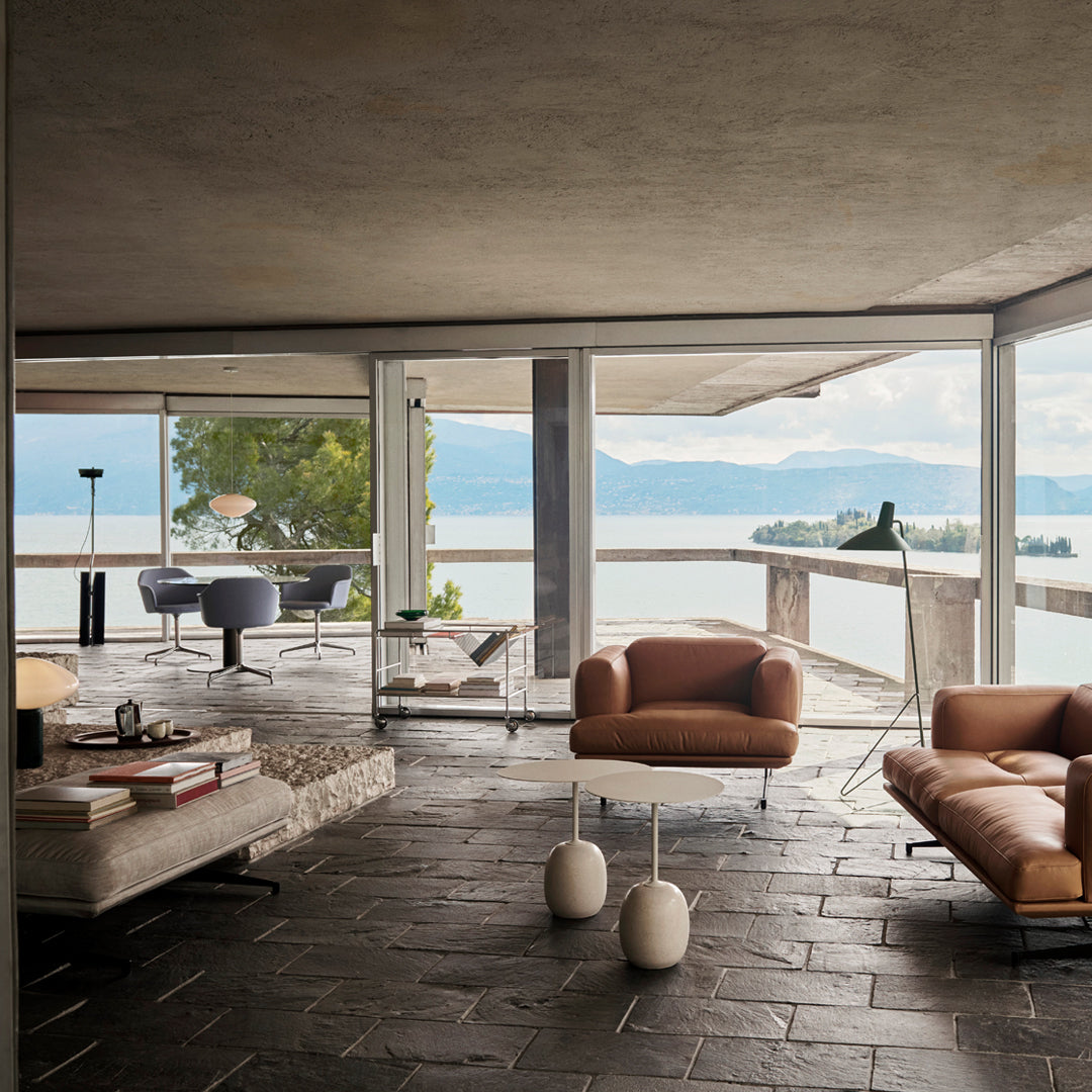 Modern living room with brown leather sofas, gray stone flooring, and large windows showcasing a scenic view.