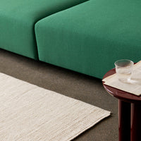 Green upholstered sofa with a textured, plain pattern, complemented by a light beige woven rug.