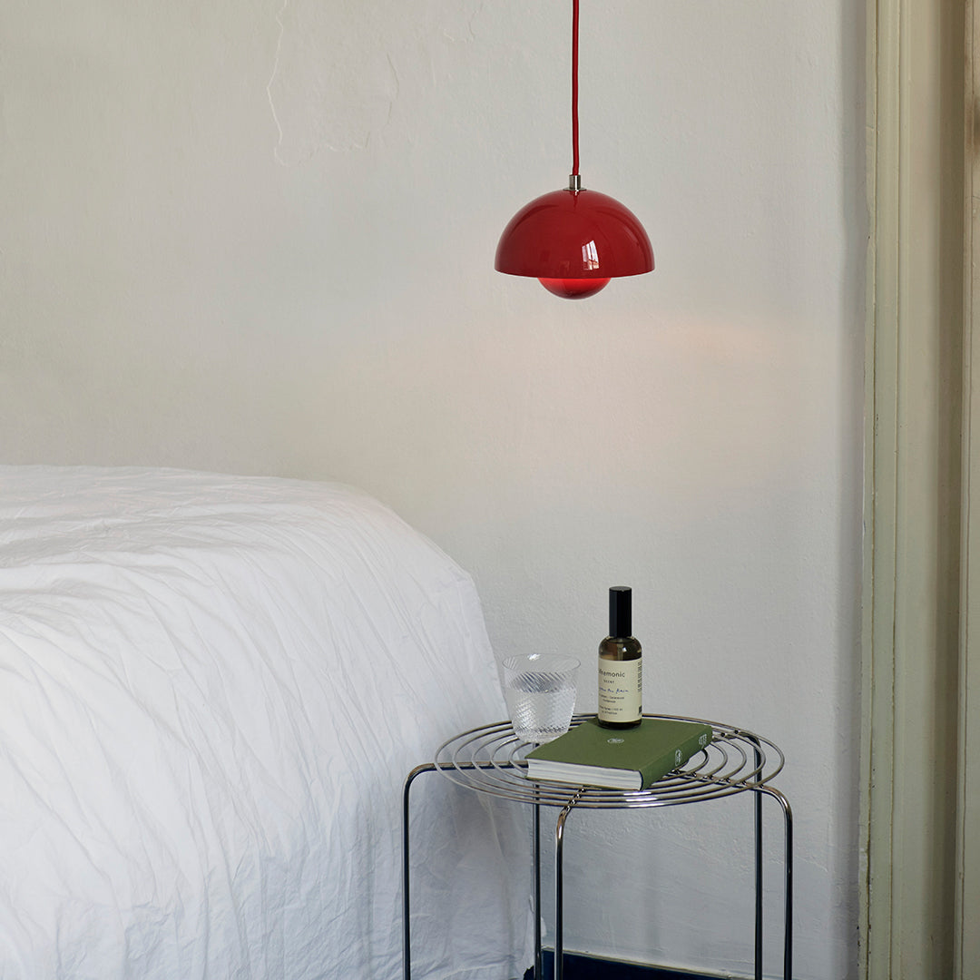 Red dome pendant light hung above a minimalist table with a green book and a glass, against a soft white wall.