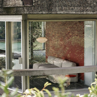 Modern lounge featuring a textured red wall, sleek gray sofa, and vibrant accents, surrounded by large glass windows.