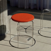 Bright orange upholstered seat on a sleek chrome base, set against a minimalist background.