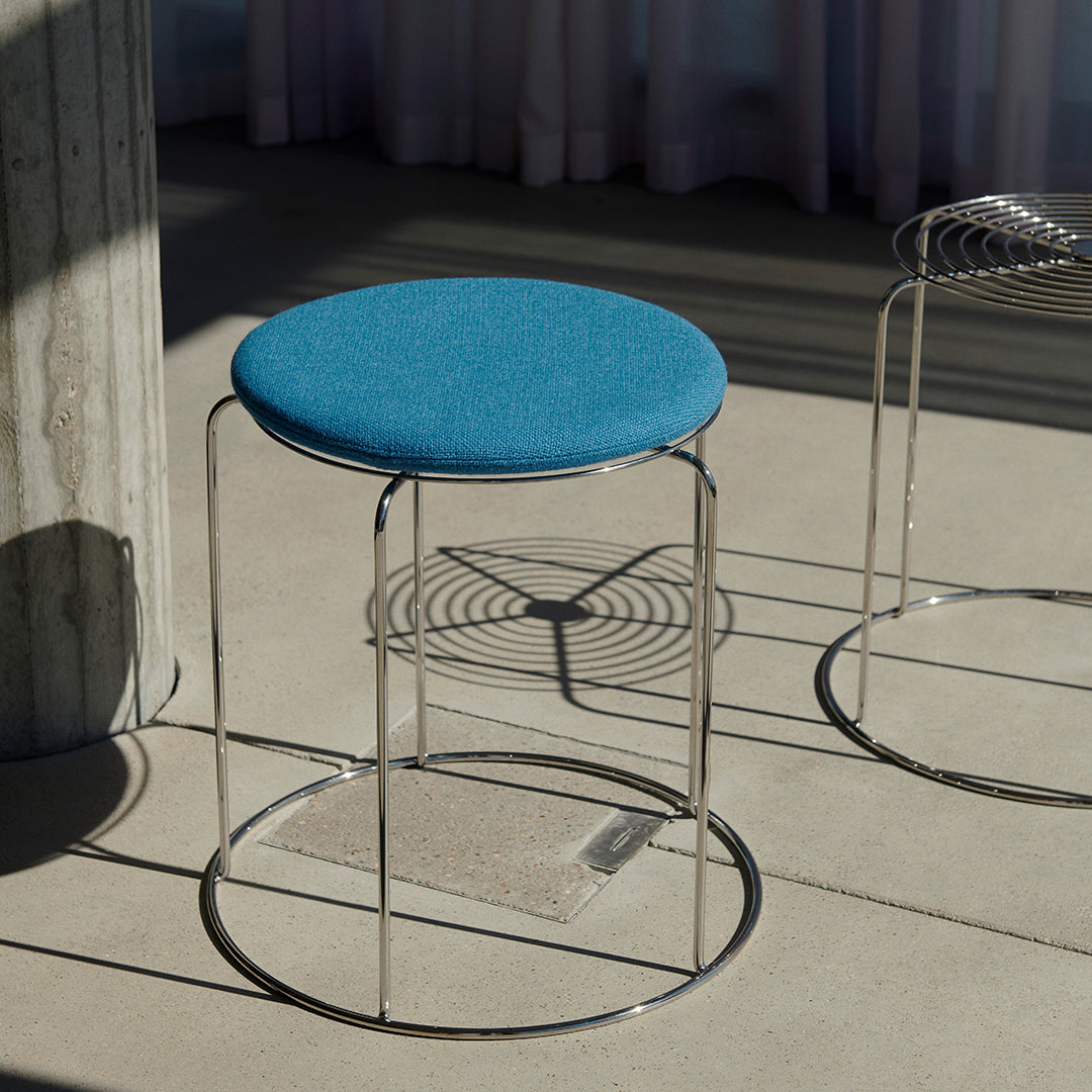 Blue upholstered stool with a sleek chrome base and circular design, perfect for modern decor.
