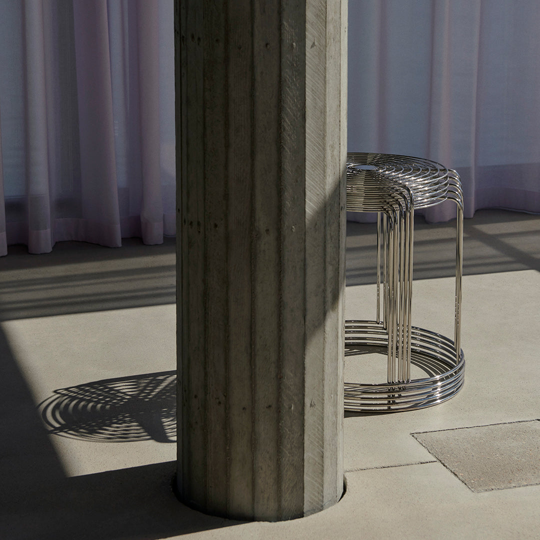 Concrete column and metallic wire stool with shadows contrasting against a soft pastel backdrop. Modern and minimal design.