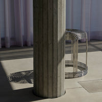 Concrete column and metallic wire stool with shadows contrasting against a soft pastel backdrop. Modern and minimal design.