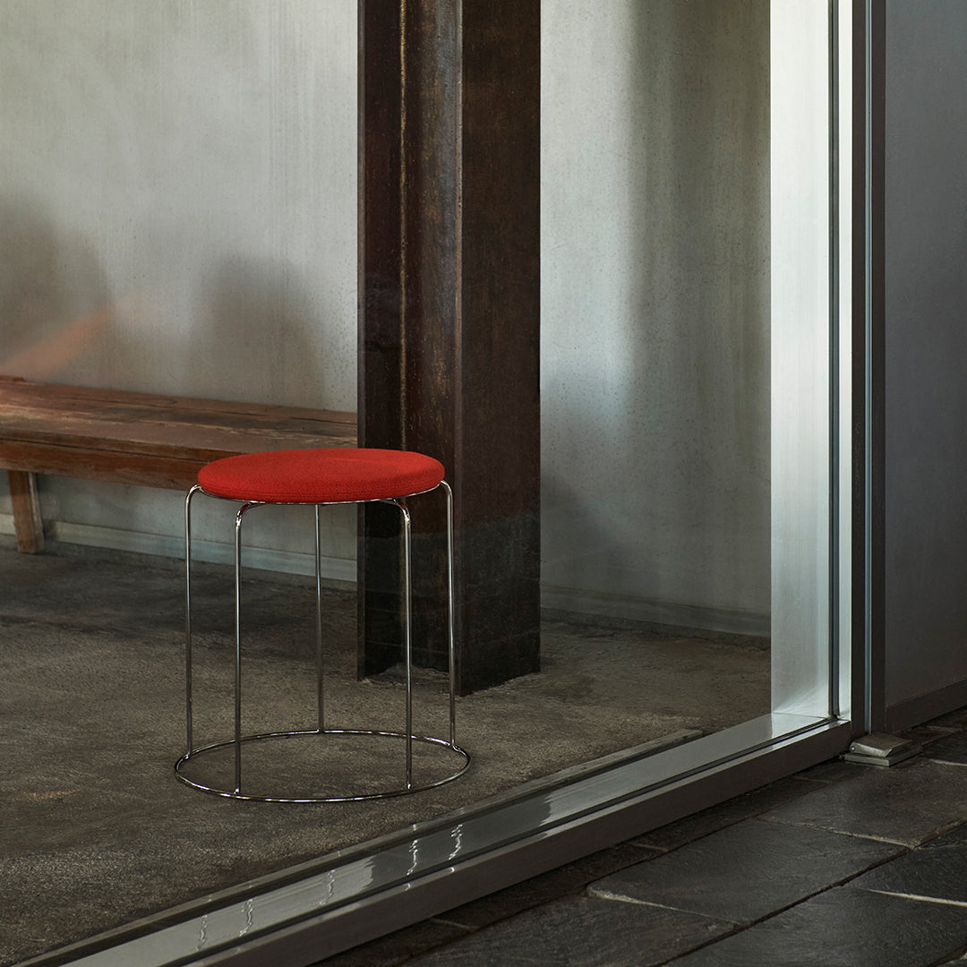 Red upholstered stool with a sleek chrome base, set against a neutral backdrop and modern materials.