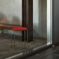 Red upholstered stool with a sleek chrome base, set against a neutral backdrop and modern materials.