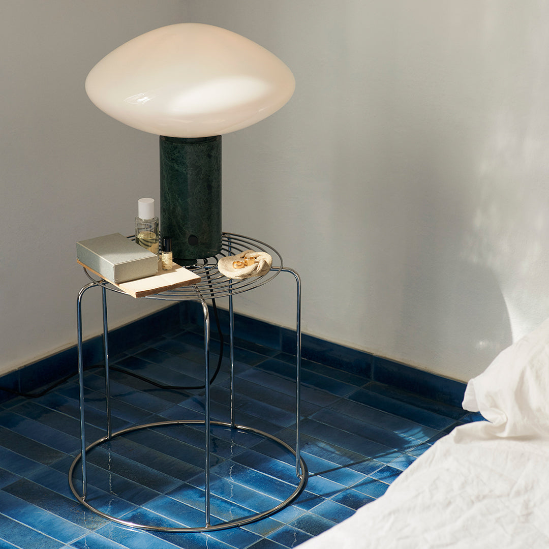"Stylish round lamp with a translucent white shade, accented by a green base and set against blue tiled flooring."