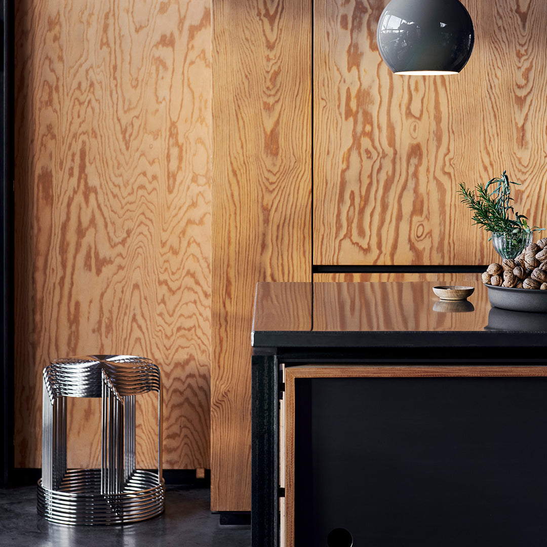 Modern minimalist decor featuring warm wood tones, sleek black surfaces, and a metallic patterned accent stool.