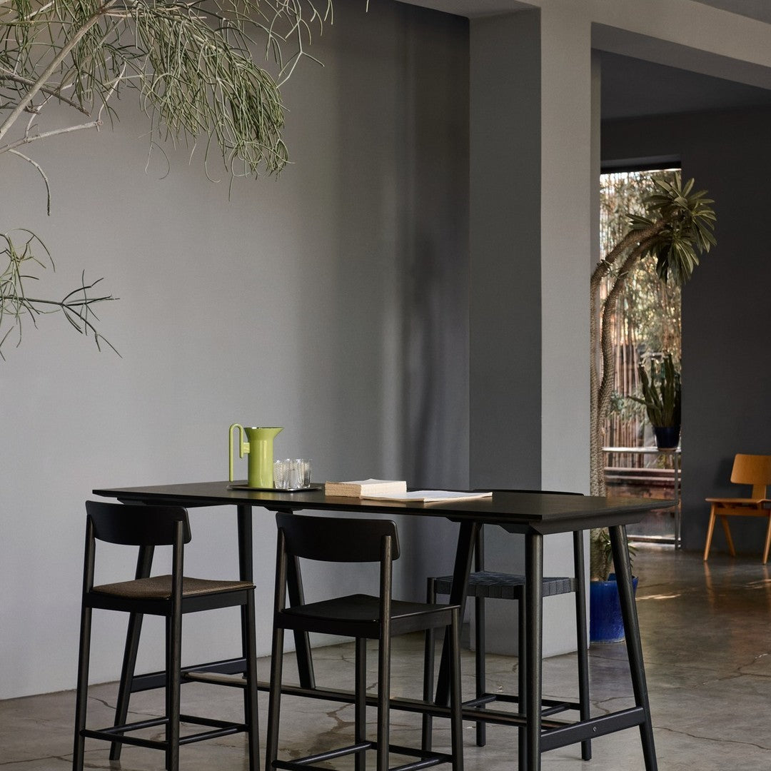 Modern black bar table with natural wood accents, set against muted gray walls and vibrant green and yellow accents.