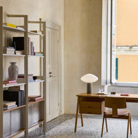 Neutral tones with pops of pink and teal, featuring a light wood desk, grey vase, and decorative books.